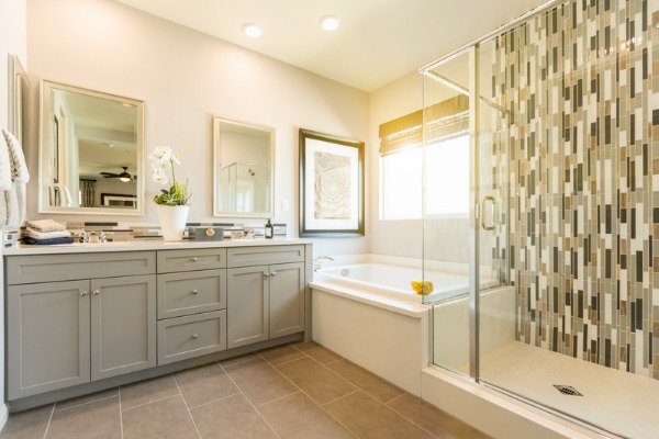 The image shows a beautiful custom master bathroom in Tega Cay, featuring a glass-enclosed shower and a bathtub. The shower is spacious and modern, with a glass enclosure that provides a sense of openness and transparency. The bathtub is positioned next to the shower, creating a cohesive and functional layout. The overall design is elegant and sophisticated, with neutral tones and minimalist fixtures that create a sense of tranquility and relaxation.