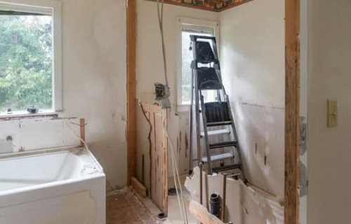 Image of a bathroom in Fort Mill, undergoing renovation and in the process of being stripped down. The walls are bare, and the fixtures, including the bathtub surround and shower, have been removed, leaving behind only the framework. The space is being prepared for a complete remodel and transformation to create a new and modern bathroom.