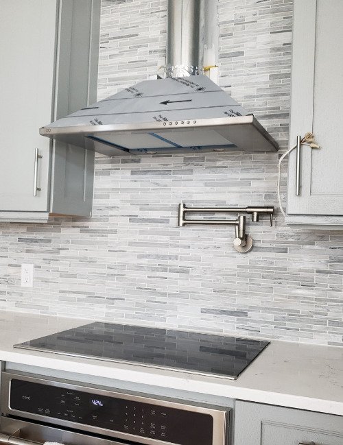 Image of a beautifully designed kitchen backsplash in Fort Mill, SC, showcasing a mix of light gray and white tiles. The backsplash features a stunning tile work design that adds a modern and elegant touch to the kitchen. The high-quality materials and expert craftsmanship create a polished and seamless finish, enhancing the overall look and feel of the kitchen space.