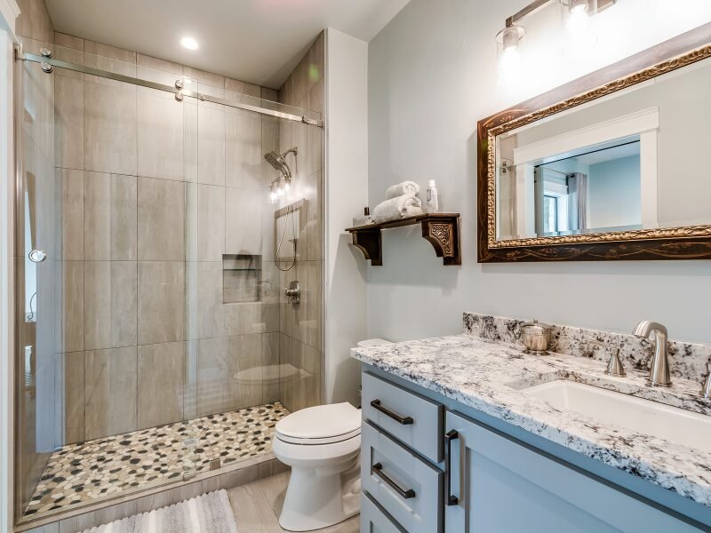 Walk-in shower with large tan wall tiles and pebble tile floor after a tub-to-shower conversion in Fort Mill, SC.